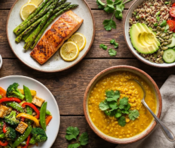 Widok z góry na zdrowe posiłki diety przeciwzapalnej: łosoś ze szparagami, sałatka z quinoa i awokado, tofu z warzywami oraz zupa z soczewicy na drewnianym stole.